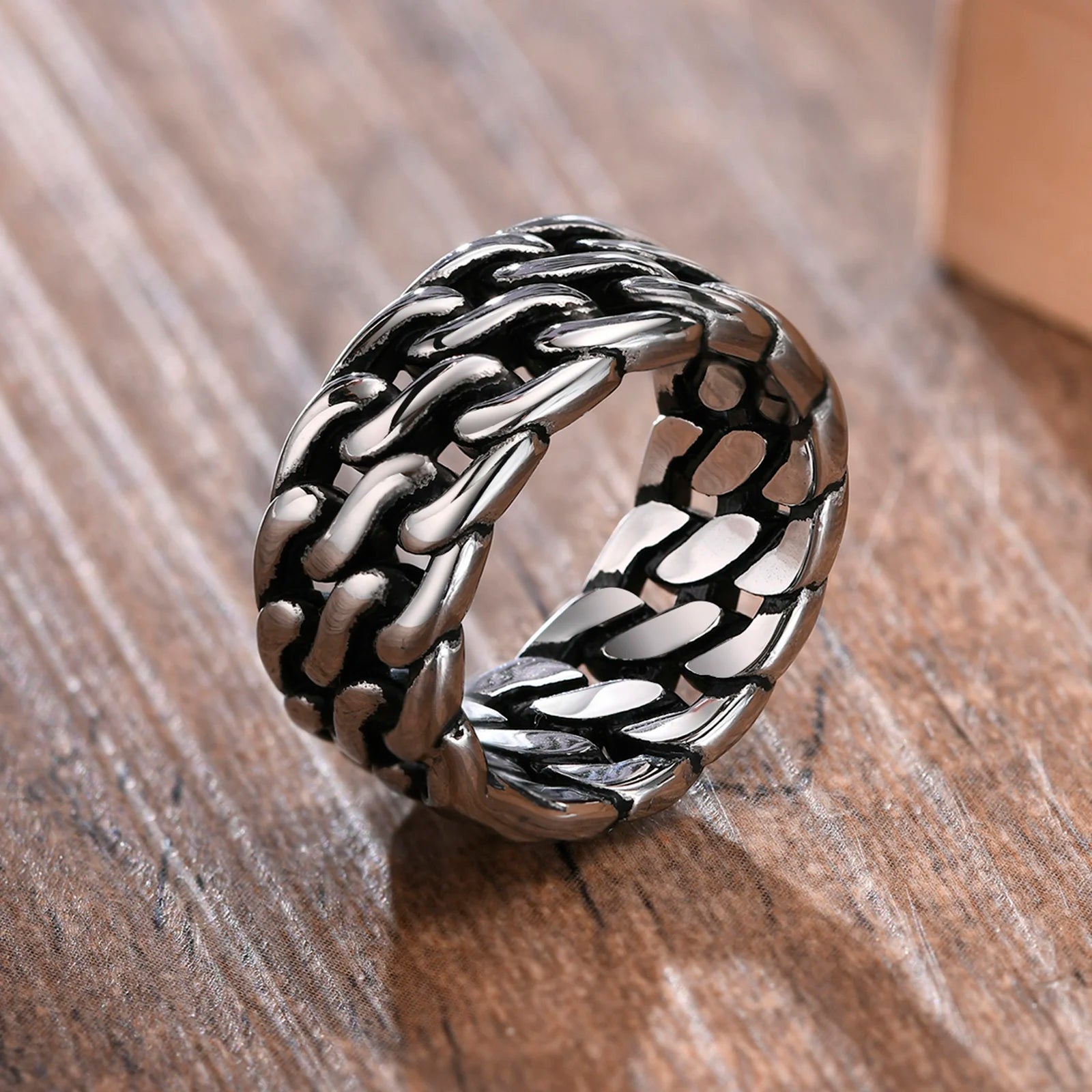 Freigestellter, breiter Edelstahl-Panzerketten-Ring (Silber) in einer leicht gekippten Ansicht auf einem Holzuntergrund.