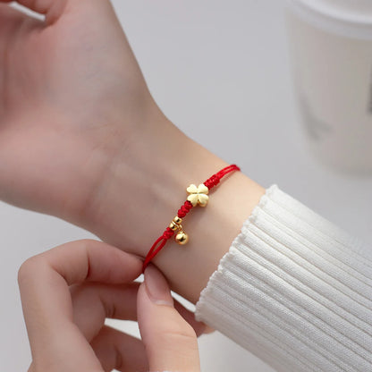 Model trägt das rote Kordelarmband mit vergoldetem Kleeblatt und Glöckchen-Anhänger elegant am Handgelenk.