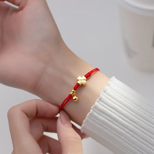 Model trägt das rote Kordelarmband mit vergoldetem Kleeblatt und Glöckchen-Anhänger elegant am Handgelenk.