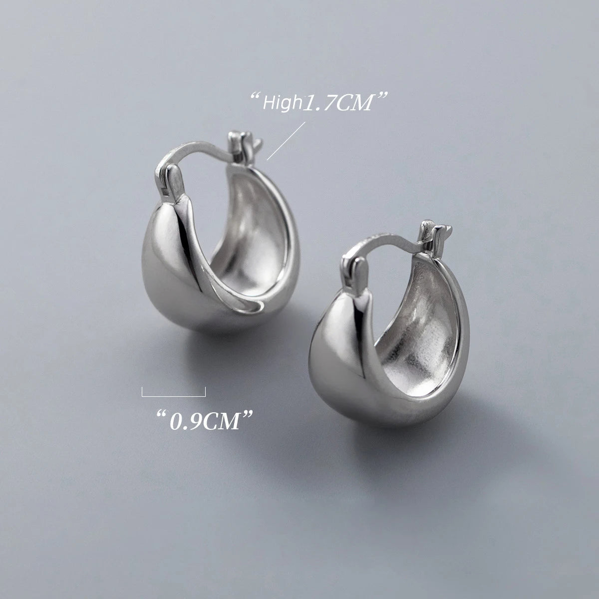 Produktbild von zwei glänzenden, bauchigen Creolen-Ohrringen aus 925er Silber auf grauem Hintergrund, mit Maßangaben für Höhe (1.7CM) und Breite (0.9CM).