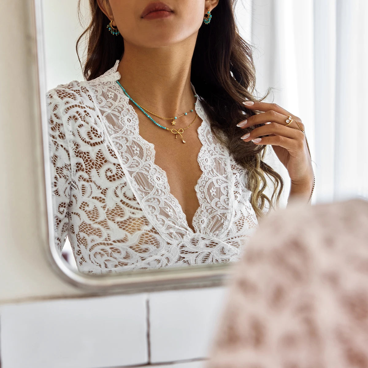 Modisches Layering mit zwei Halsketten: Eine Kette mit türkisfarbenen Perlen kombiniert mit einer goldenen Kette mit Schleifen-Anhänger. Getragen zu einem weißen Spitzen-Top.