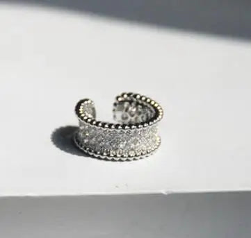 Ein breiter, offener Ring mit silberfarbenem Finish, der durchgehend mit klaren Zirkonia-Steinen besetzt ist und durch die punktierte Textur an den Rändern einen modernen Look erhält.