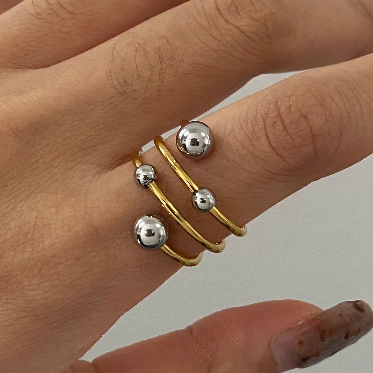 „Moderner, mehrreihiger Wickelring aus goldfarbenem Edelstahl mit silbernen Akzentkugeln an einer Hand getragen.“