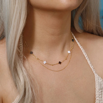 Model trägt doppelte, 14K Gold vergoldete Halskette aus 925er Sterling Silber mit beigen und schwarzen Kleeblättern.