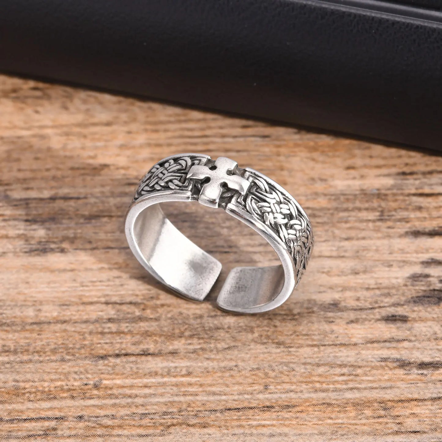 Freigestellter, silberfarbener Edelstahl-Ring mit Kreuz-Muster (Seitenansicht), liegend auf einer Holzberfläche.