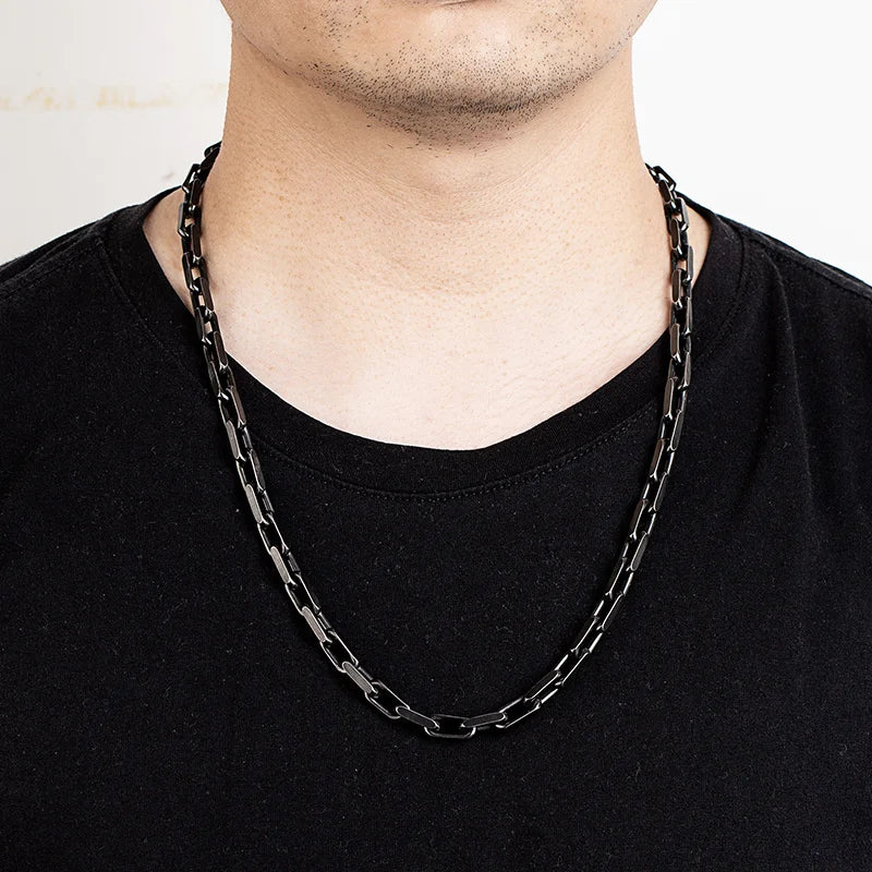 Ein Mann trägt die lange, schwarze Edelstahl-Gliederkette im Vintage-Stil über einem schwarzen T-Shirt. Die Kette liegt locker auf der Brust.