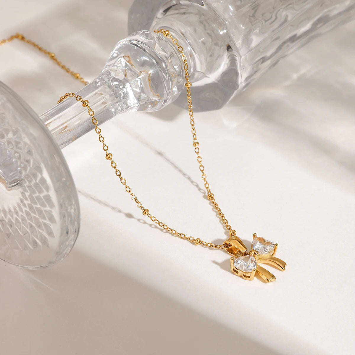 Detailansicht einer goldenen Kügelchenkette mit strahlendem Schleifen-Anhänger an einem verzierten Glas