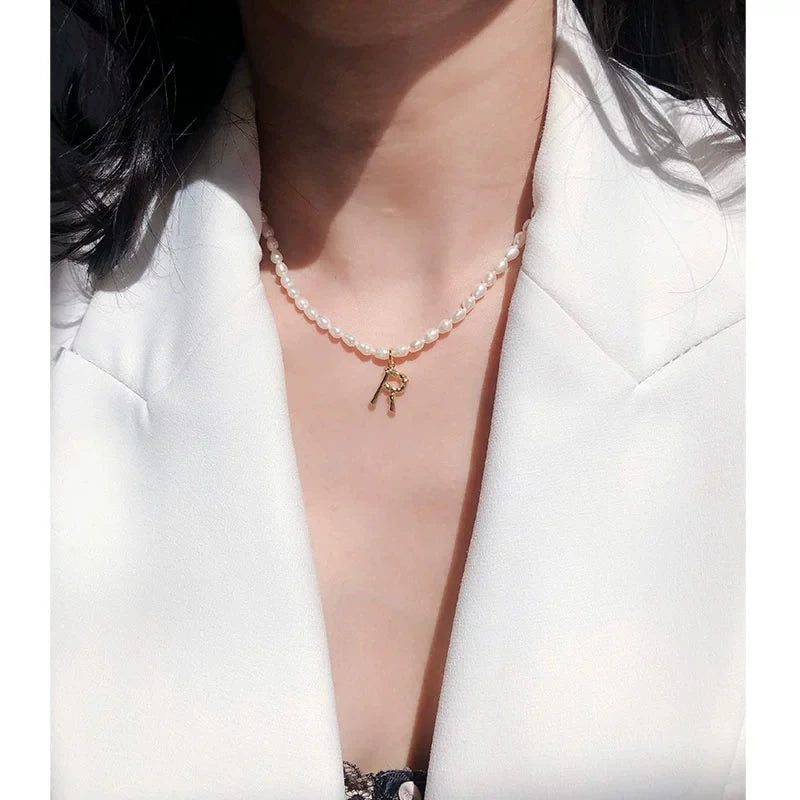 Tragestyling: Kurze Süßwasserperlenkette mit vergoldetem Buchstabe-R-Anhänger zu einem weißen Blazer.