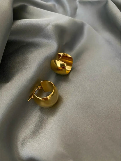 Detailaufnahme von zwei massiven, glänzenden 18K vergoldeten Creolen (Mini-Hoops) auf einem grauen Seidenstoff.