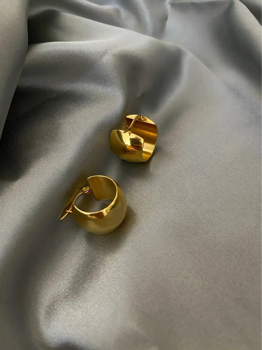 Detailaufnahme von zwei massiven, glänzenden 18K vergoldeten Creolen (Mini-Hoops) auf einem grauen Seidenstoff.