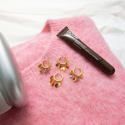 Flachbild-Produktaufnahme der goldenten Creolen mit Anhängern drapiert auf einem flauschigen rosa Pullover.