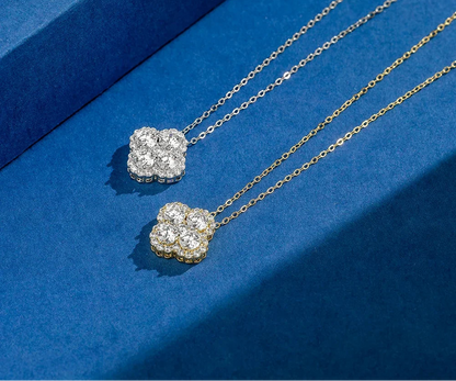 Zwei Halsketten bestehend aus 925er Silber und 14K Gold mit passenden Kleeblatt Anhängern, beide mit Zirkonia besetzt. Die Stücke liegen auf einem leuchtend blauen Untergrund.