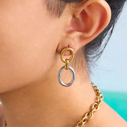 Nahaufnahme vom Ohr einer Person, die einen Ohrring aus zwei ineinandergreifenden Ringen trägt, wobei der obere Ring golden und der untere Ring silberfarben ist.