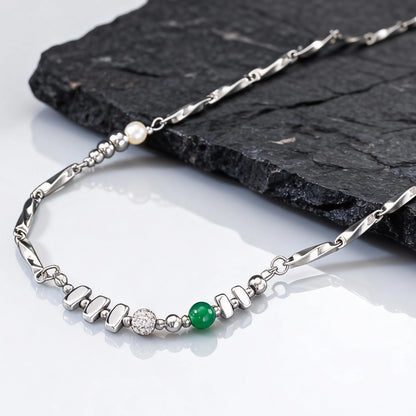 Die silberfarbene Edelstahl-Gliederkette flach drapiert, mit Fokus auf die eingefasste grüne Natursteinperle und die weiße Perle.