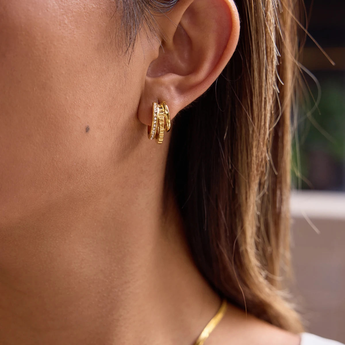 „Nahaufnahme einer Frau, die elegante, dreireihige Creolen aus 18K vergoldetem Edelstahl trägt – eine Reihe ist mit funkelnden Zirkonia-Steinen besetzt.“