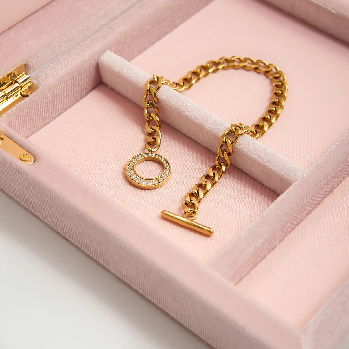 Das goldene Edelstahl-Armband liegt elegant in einem rosa Schmuckkästchen; der Fokus liegt auf der hochwertigen Verarbeitung der Kettenglieder und dem glitzernden Verschluss.