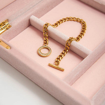 Das goldene Edelstahl-Armband liegt elegant in einem rosa Schmuckkästchen; der Fokus liegt auf der hochwertigen Verarbeitung der Kettenglieder und dem glitzernden Verschluss.