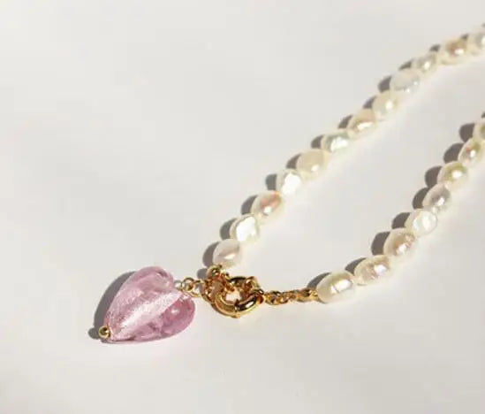 Naturperlenkette mit 18K vergoldetem Titan-Knebelverschluss und rosa Kristall-Herzanhänger auf hellem Grund.