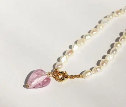 Naturperlenkette mit 18K vergoldetem Titan-Knebelverschluss und rosa Kristall-Herzanhänger auf hellem Grund.