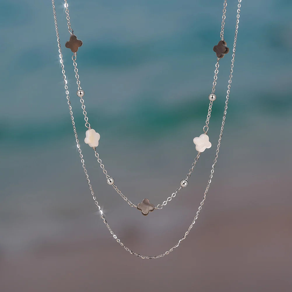 Zarte, doppelte Halskette aus 925er Silber mit Kleeblättern, am Strand oder Meer.