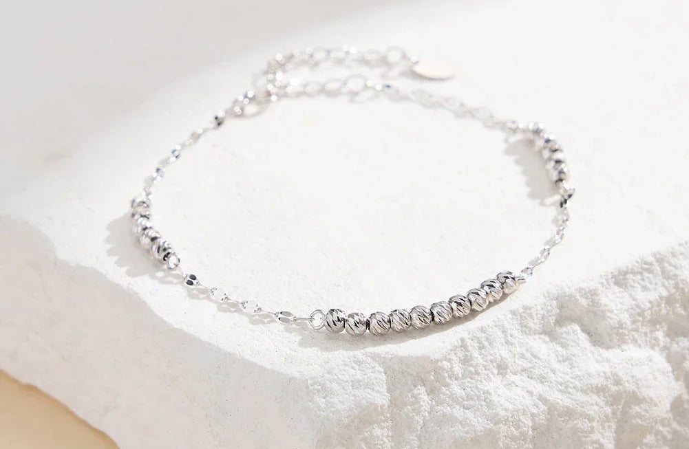 Elegantes, silbernes Armband aus 925er Sterling Silber, bestehend aus kleinen, glänzenden Kügelchen, liegend auf einer weißen, strukturierten Oberfläche.