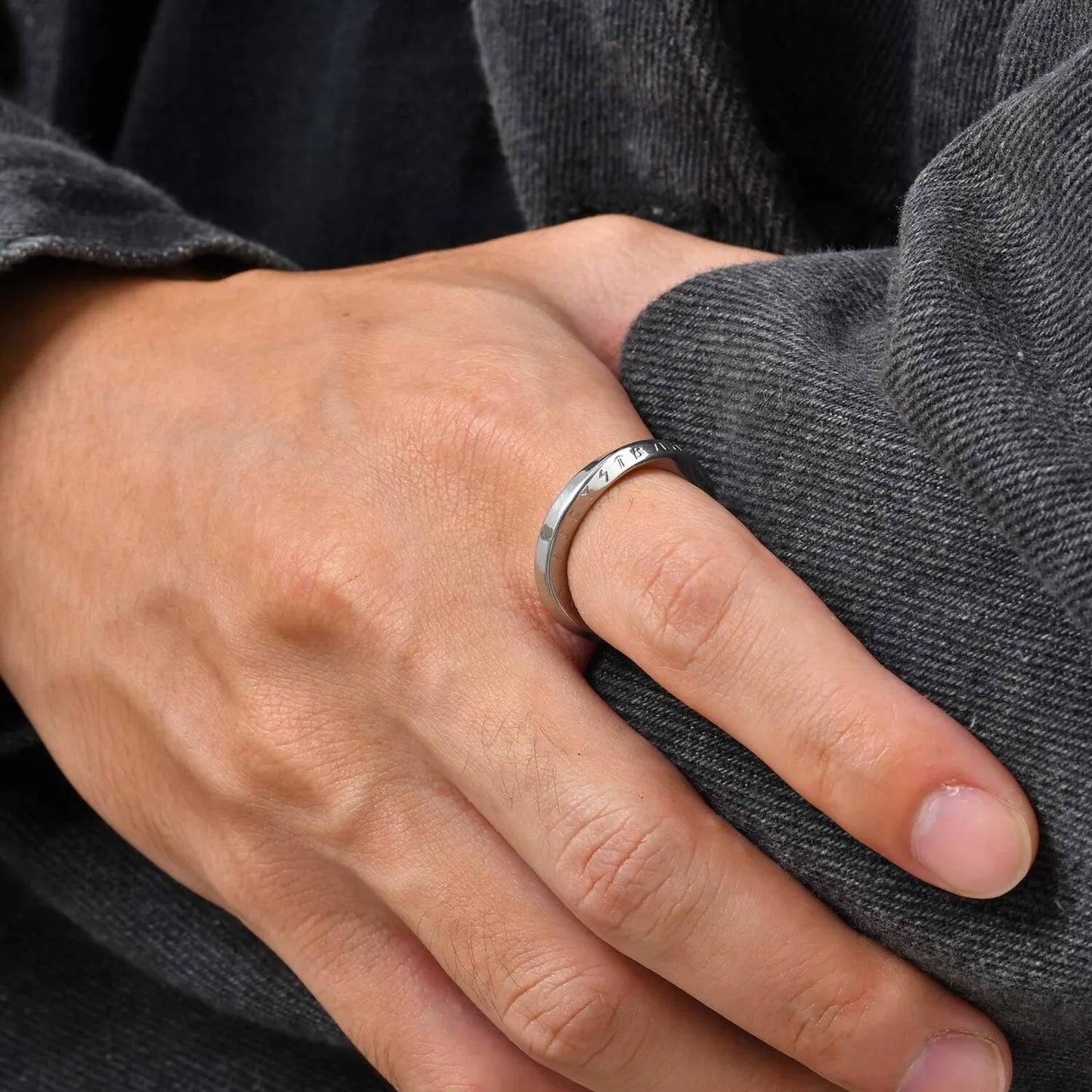 Gedrehter Edelstahlring für Damen und Herren, getragen am Zeigefinger einer Hand auf dunkelgrauem Stoff.