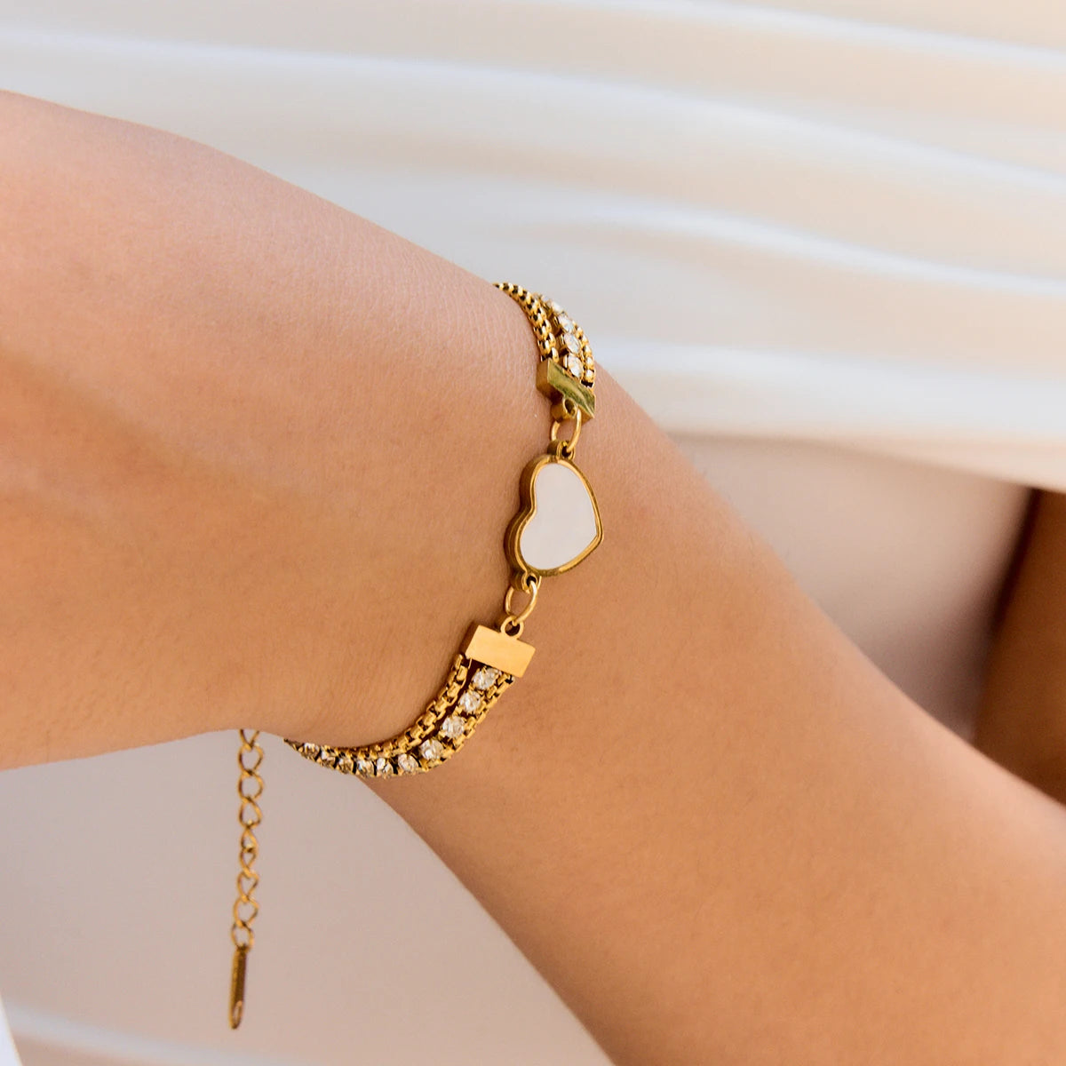 Nahaufnahme eines eleganten Damen-Armbands aus vergoldetem Edelstahl mit Perlmutt-Herz und glitzernden Schmucksteinen am Handgelenk.