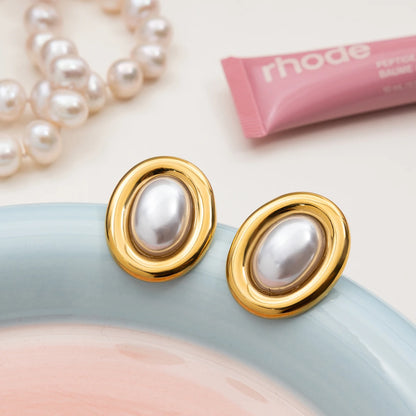 Zwei goldene Ohrstecker mit weißen Harzperlen liegen auf einem pastellfarbenen Teller, daneben ein rosafarbener Lippenstift. Eine schicke Schmuckszene für einen Beauty-orientierten Kontext.