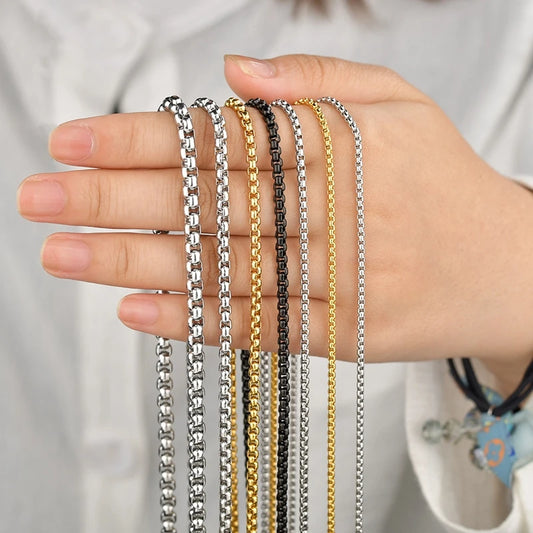 Fünf verschiedene Edelstahl-Boxketten (Venezianerketten) in den Farben Silber, Gold und Schwarz in der Hand gehalten, um die verschiedenen Stärken und Oberflächen zur Schau zu stellen.