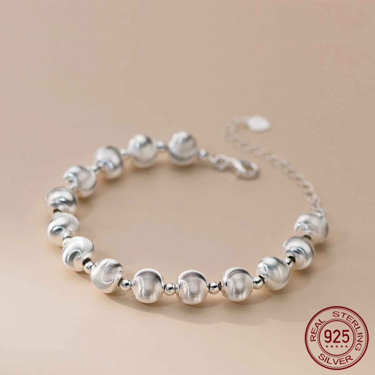Nahaufnahme eines glänzenden Armbandes aus 925er Sterling Silber, bestehend aus mattierten und glänzenden Kugelperlen, mit einem verstellbaren Kettenverschluss. Ein "925 STERLING SILVER" Siegel ist sichtbar.