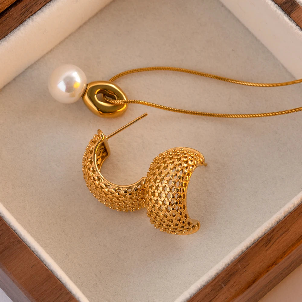 Goldene Edelstahl-Creole in Gitter-Optik neben einer Perlenkette in einer Schmuckschatulle präsentiert.