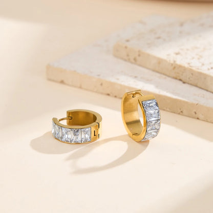 Nahaufnahme von goldenen Edelstahl-Ohrringen mit Zirkonia-Besatz und 18K Gold auf dekorativem Untergrund.