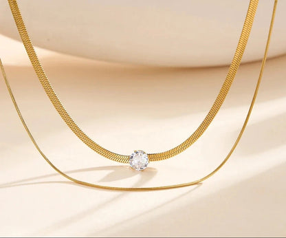 Nahaufnahme der 18K vergoldeten, zweireihigen Edelstahl-Kette mit funkelndem Zirkonia-Anhänger vor hellem Hintergrund.
