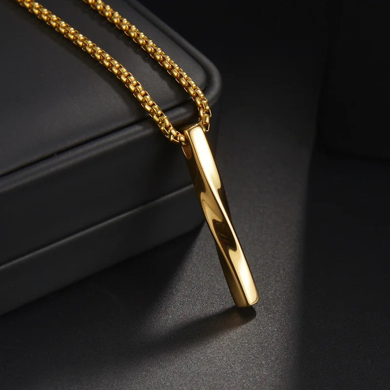  Nahaufnahme einer goldfarbenen Edelstahl-Kette mit einem glänzenden, verdrehten Stab-Anhänger (Bar-Anhänger) auf einem dunklen Hintergrund, der den Glanz hervorhebt.