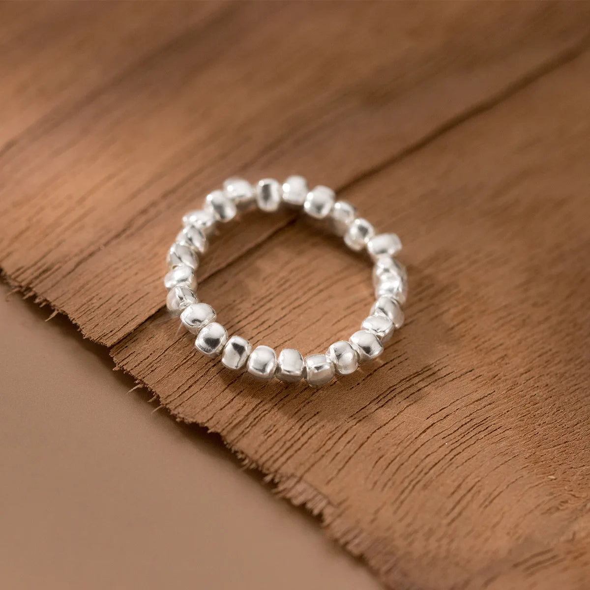 Offener 925 Silber Ring mit unregelmäßiger, gehämmerter Textur, ohne Perle, auf einem braun-beigen Hintergrund.