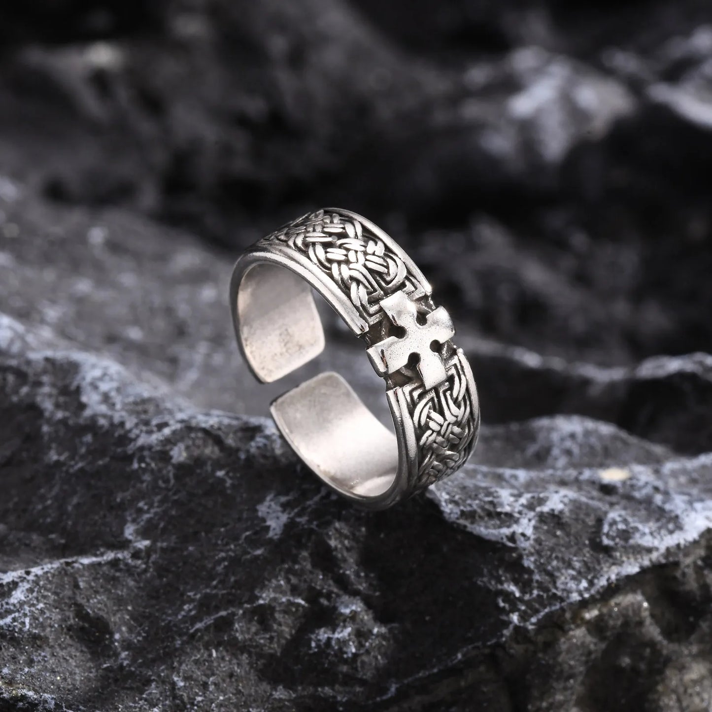 Freigestellter silberfarbener Edelstahl-Ring mit Kreuz-Muster, liegend auf dunklem, rustikalem Felsen, um das Finish hervorzuheben.