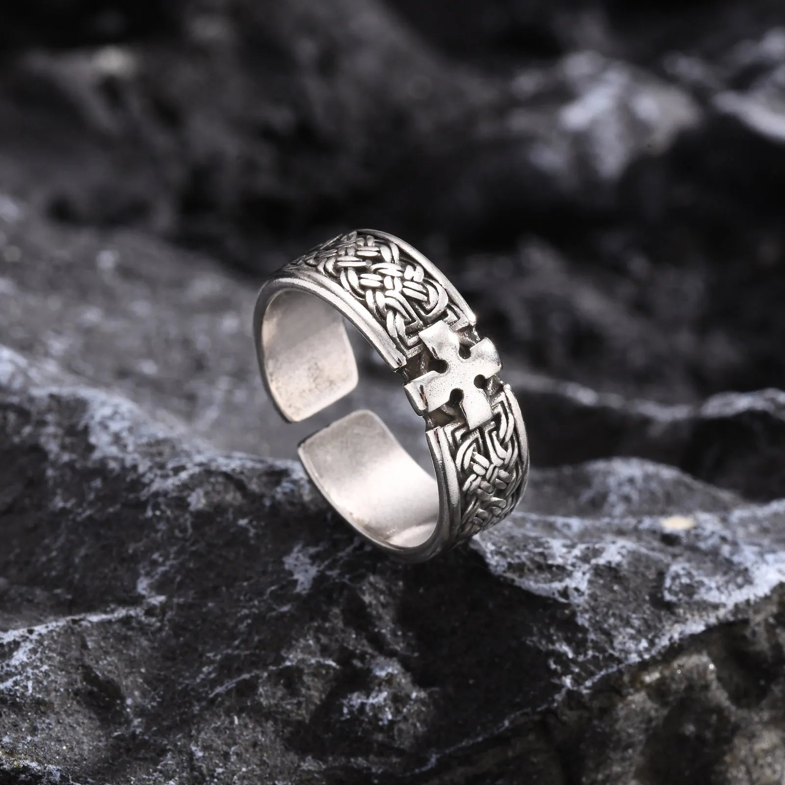 Freigestellter silberfarbener Edelstahl-Ring mit Kreuz-Muster, liegend auf dunklem, rustikalem Felsen, um das Finish hervorzuheben.