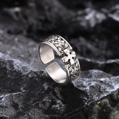 Freigestellter silberfarbener Edelstahl-Ring mit Kreuz-Muster, liegend auf dunklem, rustikalem Felsen, um das Finish hervorzuheben.