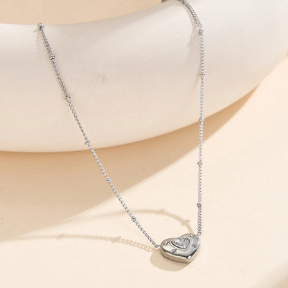 Silberne Edelstahl-Halskette mit Zirkonia-Herzanhänger elegant auf hellem Dekorationsstein präsentiert.