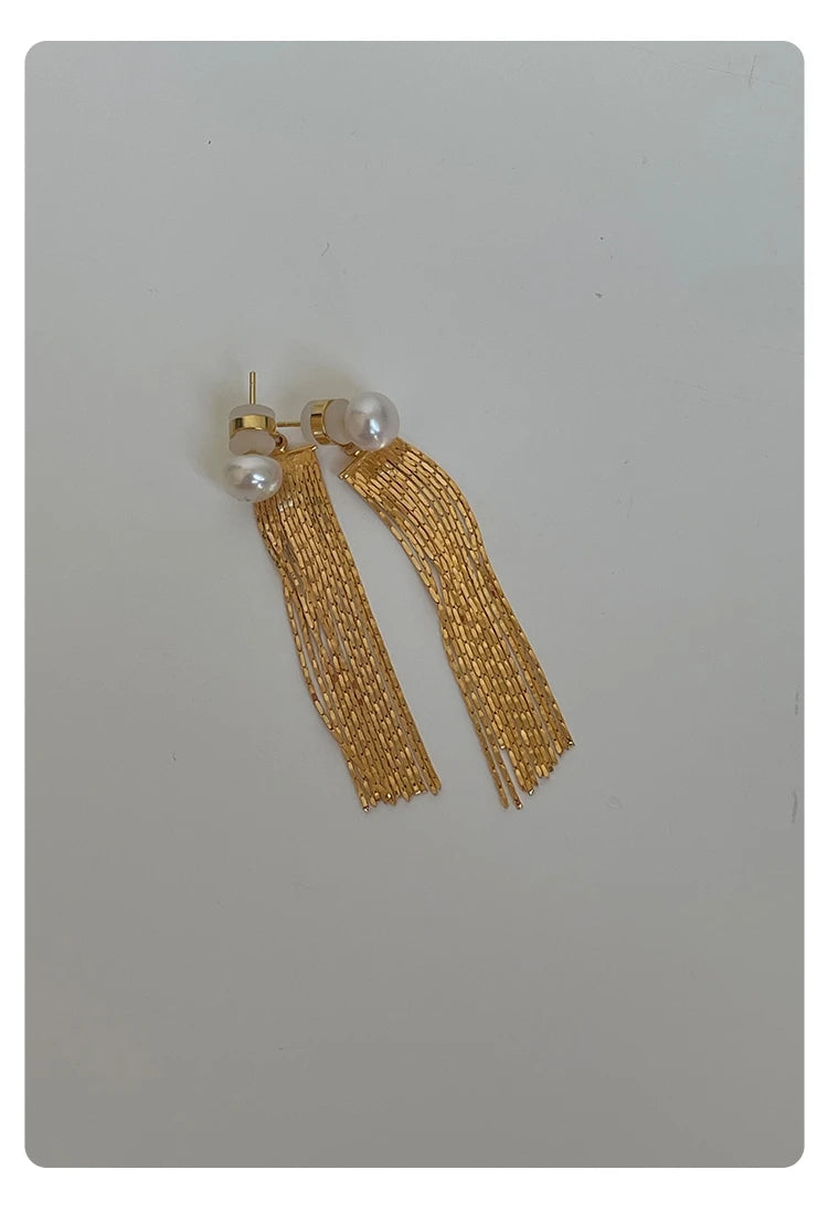 Ein Paar der goldfarbenen Ohrringe liegt flach auf einem neutralen Hintergrund, was das symmetrische Design und den Glanz des 14k vergoldeten Messings neben den weißen Perlen betont.