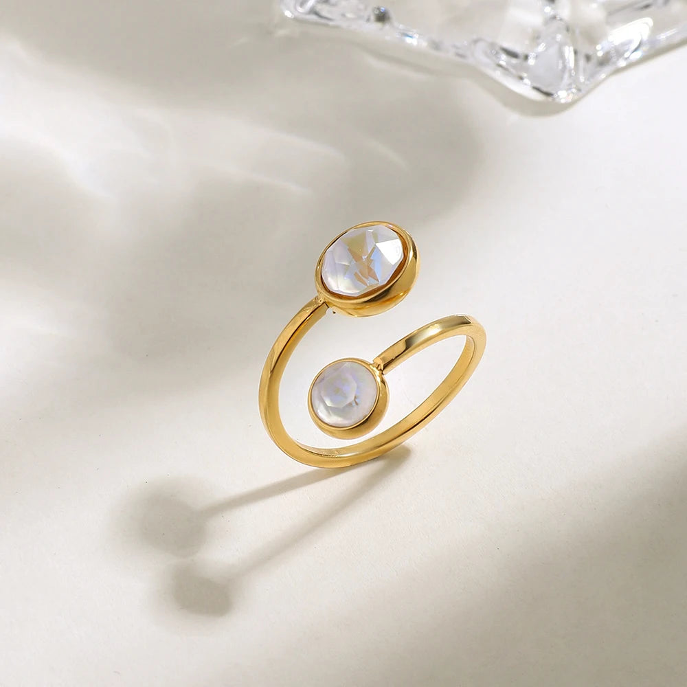 Moderner, offener Ring aus 18K vergoldetem Edelstahl mit zwei unterschiedlich großen, runden Elementen in Perlmutt-Optik, stehend fotografiert mit weichem Schatten.