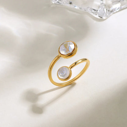 Moderner, offener Ring aus 18K vergoldetem Edelstahl mit zwei unterschiedlich großen, runden Elementen in Perlmutt-Optik, stehend fotografiert mit weichem Schatten.
