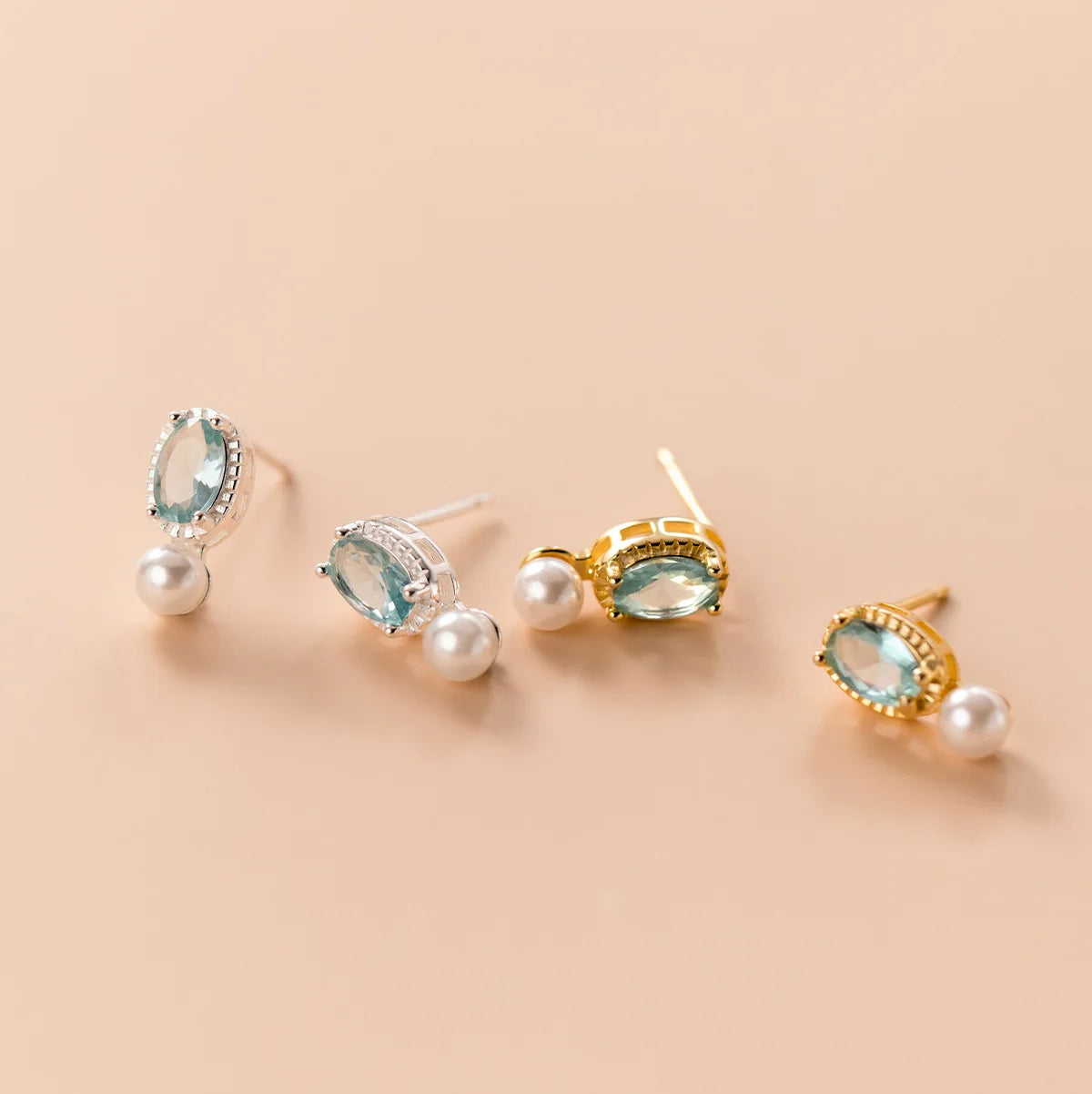 Produktübersicht der Perlenohrringe in zwei Varianten: 925er Silber naturbelassen und mit 18K Gelbgold vergoldet, jeweils mit hellblauem Zirkonia-Stein.
