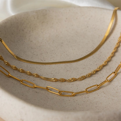 Schmuck-Flatlay der vergoldeten Edelstahlketten auf beigem Untergrund mit sanftem Schattenwurf.
