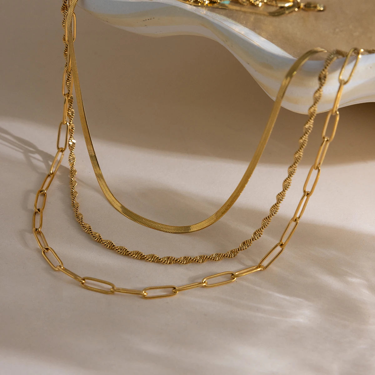 Drei goldene Edelstahlketten mit 18K Gold im Layering-Stil ästhetisch arrangiert in einer flachen Schale.