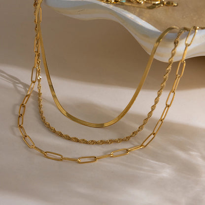 Drei goldene Edelstahlketten mit 18K Gold im Layering-Stil ästhetisch arrangiert in einer flachen Schale.