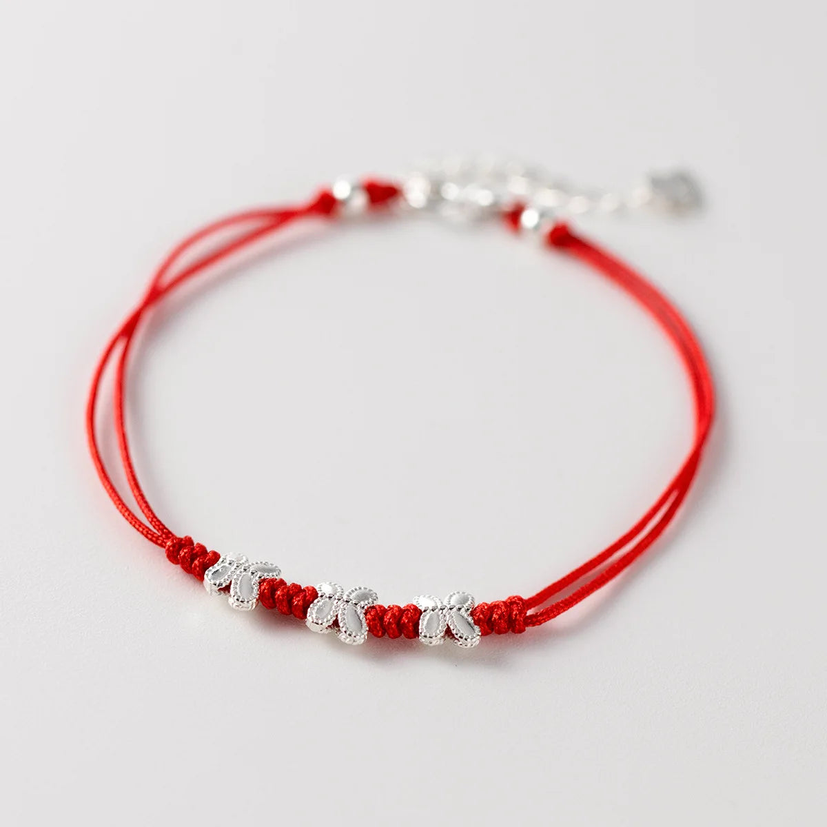 Nahaufnahme eines roten Kordelarmbands mit drei filigranen Schmetterlings-Anhängern aus 925er Sterling Silber auf weißem Hintergrund.