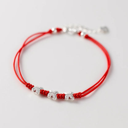 Nahaufnahme eines roten Kordelarmbands mit drei filigranen Schmetterlings-Anhängern aus 925er Sterling Silber auf weißem Hintergrund.