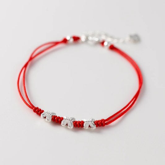 Nahaufnahme eines roten Kordelarmbands mit drei filigranen Schmetterlings-Anhängern aus 925er Sterling Silber auf weißem Hintergrund.