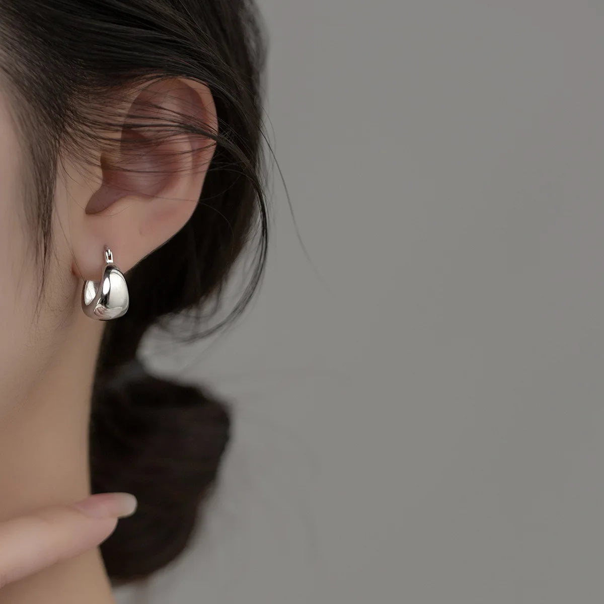 Seitenansicht einer Frau, die einen kleinen, glänzenden, bauchigen Creolen-Ohrring aus 925er Silber trägt.